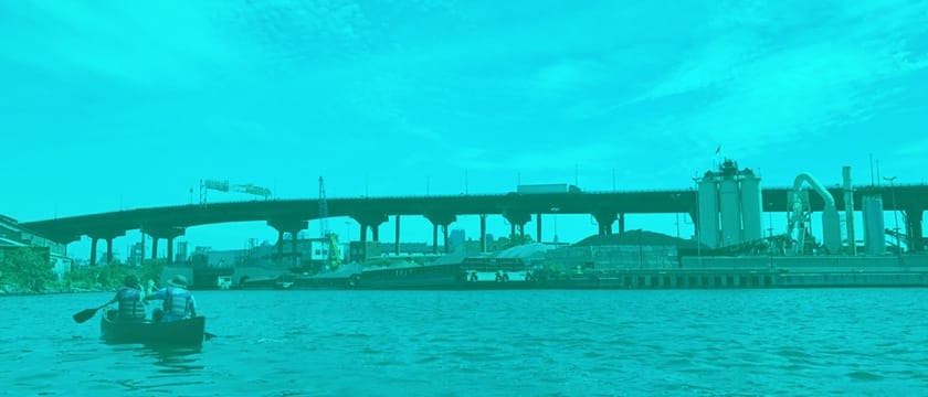 a two person kayak, paddling in front of an overpass in the gowanus canal